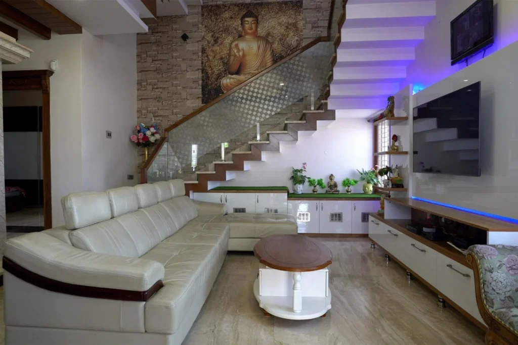Modern living room interior with L-shaped sofa, TV unit, staircase design, and Buddha wall art